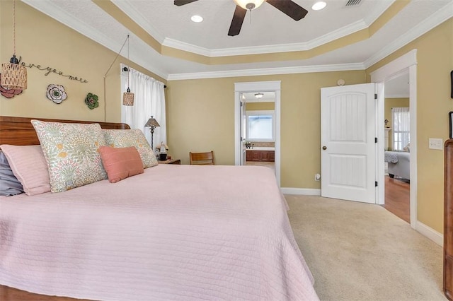 carpeted bedroom with a tray ceiling, ensuite bath, ceiling fan, and ornamental molding