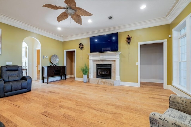 living room with ceiling fan, ornamental molding, a tiled fireplace, and light hardwood / wood-style flooring