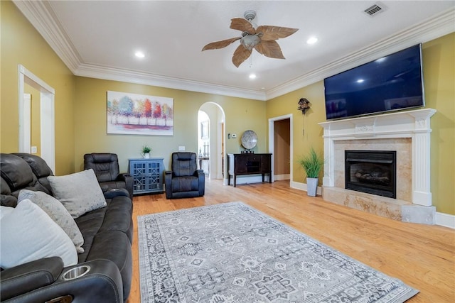 living room with wood-type flooring, ornamental molding, ceiling fan, and a high end fireplace