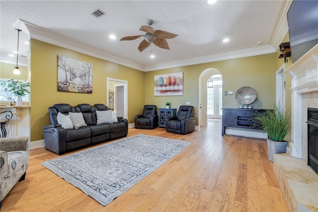 living room with a tile fireplace, ornamental molding, ceiling fan, and light hardwood / wood-style flooring