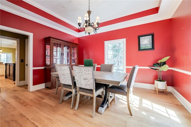 dining space with a raised ceiling, crown molding, light wood-type flooring, and an inviting chandelier