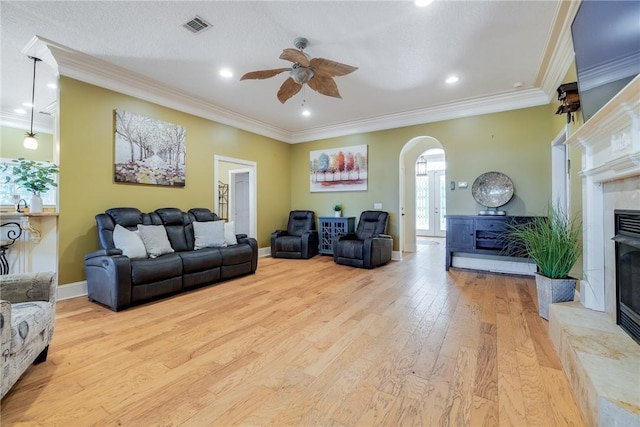 living room featuring a tiled fireplace, ornamental molding, light hardwood / wood-style floors, and ceiling fan