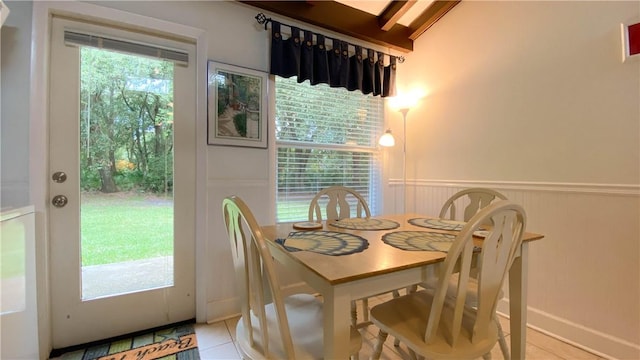 tiled dining space featuring beam ceiling and a wainscoted wall