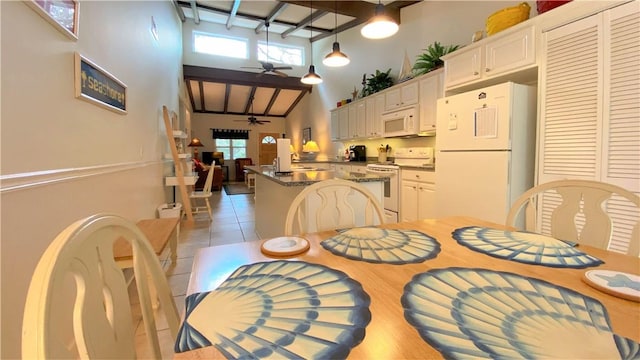 dining room with a healthy amount of sunlight, a ceiling fan, light tile patterned flooring, and a towering ceiling