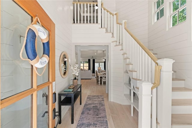 foyer entrance with wood walls, stairway, wood finished floors, and a towering ceiling