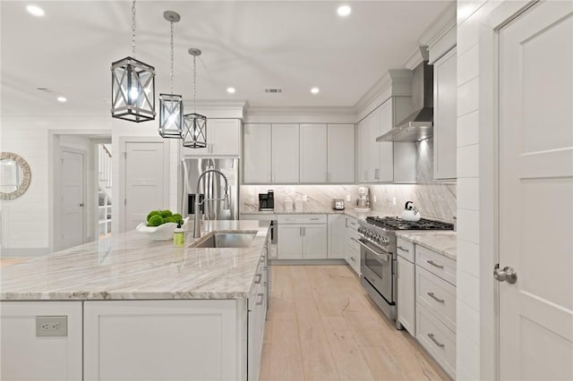 kitchen featuring a sink, stainless steel appliances, a center island with sink, wall chimney range hood, and white cabinets
