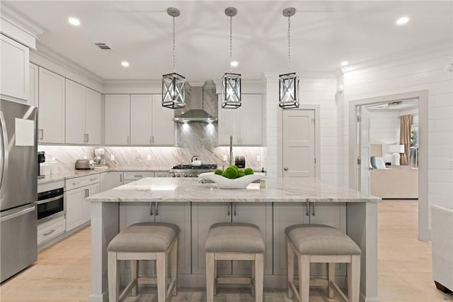 kitchen with appliances with stainless steel finishes, visible vents, ornamental molding, wall chimney exhaust hood, and backsplash
