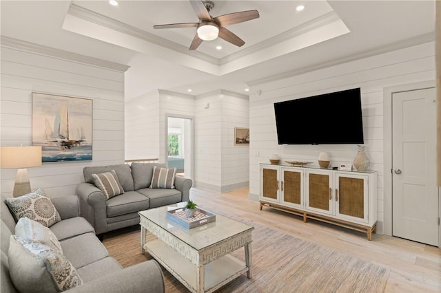 living room with light wood-style floors, wood walls, a ceiling fan, crown molding, and a tray ceiling