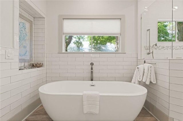 bathroom featuring tile walls, a freestanding tub, a tile shower, and plenty of natural light