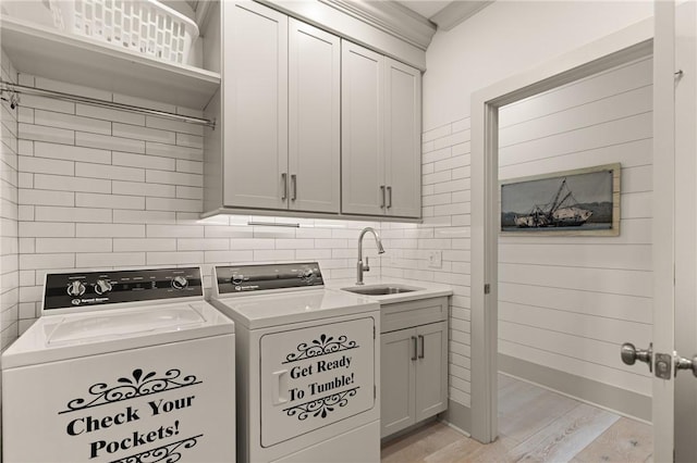 laundry area with light wood finished floors, cabinet space, a sink, independent washer and dryer, and ornamental molding
