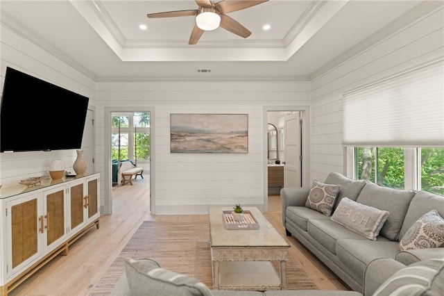 living area with ceiling fan, crown molding, light wood-style flooring, and a tray ceiling