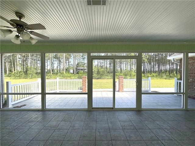 unfurnished sunroom with a ceiling fan, visible vents, and a healthy amount of sunlight