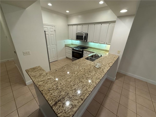 kitchen with kitchen peninsula, sink, appliances with stainless steel finishes, light stone counters, and white cabinetry