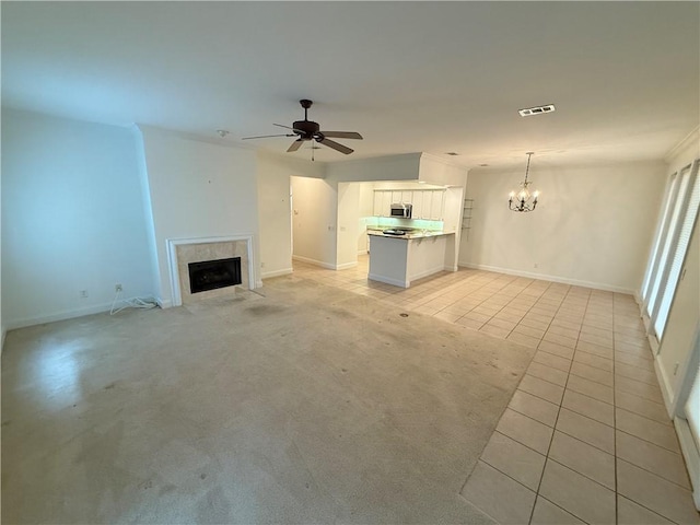 unfurnished living room with a tile fireplace, ceiling fan with notable chandelier, and light tile patterned flooring