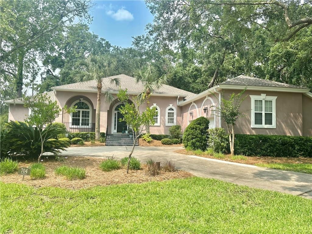 704 Dungeness, Saint Simons Island, GA 31522 - mediterranean / spanish house with stucco siding, a front lawn, concrete driveway, and covered porch