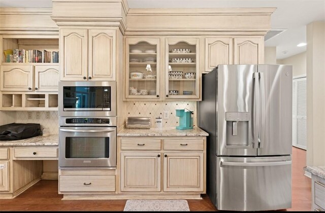 704 Dungeness, Saint Simons Island, GA 31522 - kitchen with appliances with stainless steel finishes, cream cabinetry, backsplash, glass insert cabinets, and light stone countertops