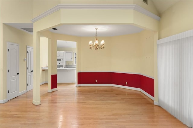 spare room featuring vaulted ceiling, a notable chandelier, and light hardwood / wood-style flooring