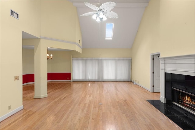 living room with ceiling fan with notable chandelier, a tile fireplace, high vaulted ceiling, and light hardwood / wood-style flooring