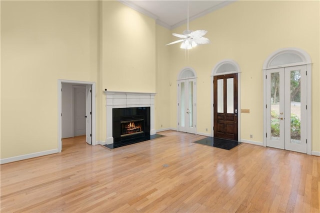 unfurnished living room featuring light hardwood / wood-style flooring, french doors, a towering ceiling, ceiling fan, and ornamental molding