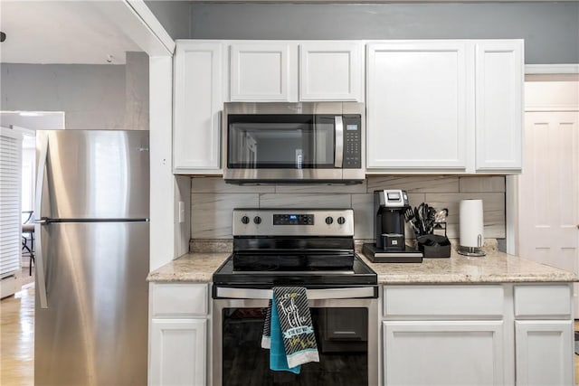 kitchen with appliances with stainless steel finishes, tasteful backsplash, white cabinets, and light stone countertops