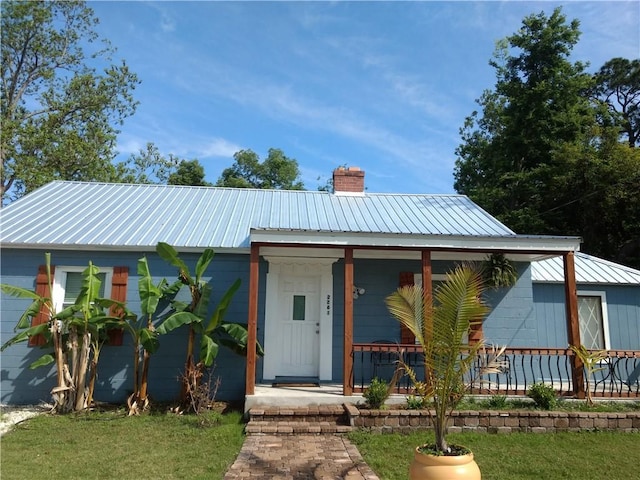 view of front of property with covered porch, a chimney, a front lawn, and metal roof