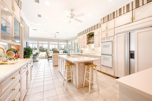 kitchen featuring ceiling fan, white double oven, a kitchen bar, a center island with sink, and light tile patterned flooring