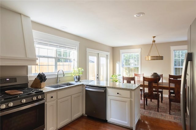 kitchen featuring a peninsula, dark wood-style flooring, a sink, appliances with stainless steel finishes, and light stone countertops