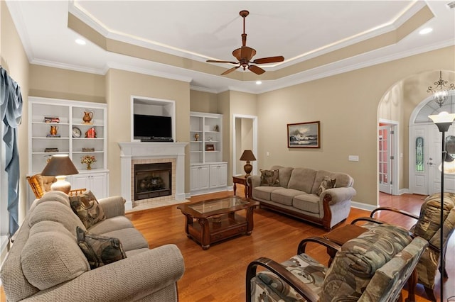 living room with ornamental molding, a tray ceiling, ceiling fan, light hardwood / wood-style floors, and a tiled fireplace