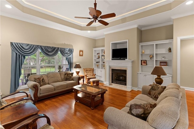 living room with hardwood / wood-style floors, ceiling fan, a raised ceiling, and a tiled fireplace