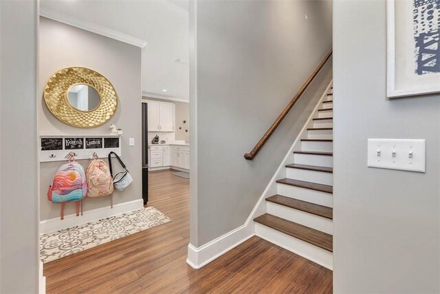 stairs with baseboards, wood finished floors, and ornamental molding