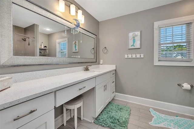bathroom with tiled shower, vanity, and baseboards