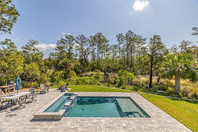 view of pool featuring a lawn, a pool with connected hot tub, and a patio