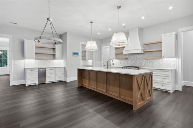 kitchen featuring hanging light fixtures, dark hardwood / wood-style floors, premium range hood, an island with sink, and white cabinets