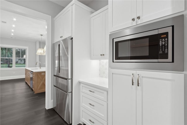 kitchen featuring white cabinets, sink, hanging light fixtures, appliances with stainless steel finishes, and dark hardwood / wood-style flooring