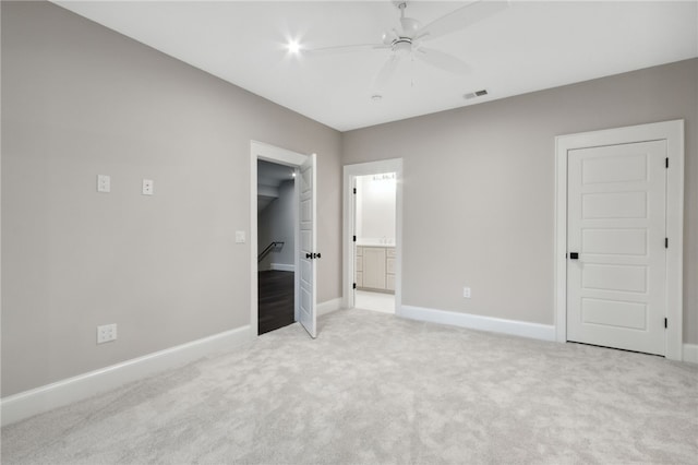 unfurnished bedroom with ceiling fan, light colored carpet, a walk in closet, and ensuite bath