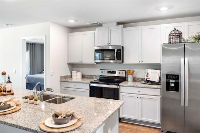 kitchen with white cabinets, sink, light stone counters, and stainless steel appliances