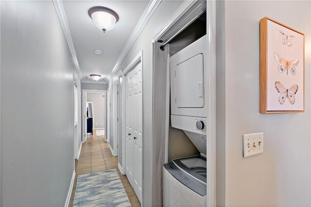 laundry area featuring crown molding, light tile patterned flooring, stacked washer / drying machine, baseboards, and laundry area