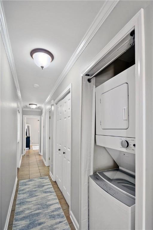 washroom featuring baseboards, stacked washer and clothes dryer, ornamental molding, and tile patterned floors