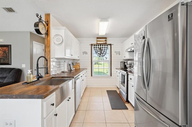 kitchen with wood walls, white cabinetry, stainless steel appliances, and light tile patterned floors