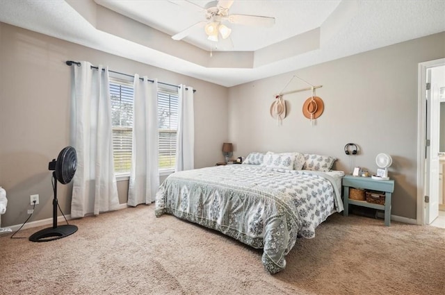 bedroom with carpet flooring, ceiling fan, ensuite bathroom, and a tray ceiling