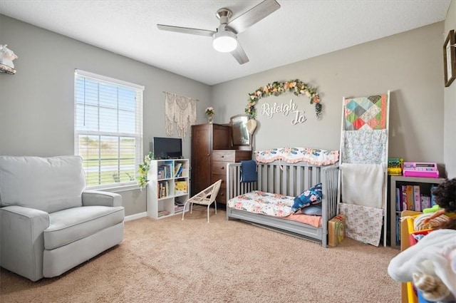 carpeted bedroom featuring a nursery area and ceiling fan