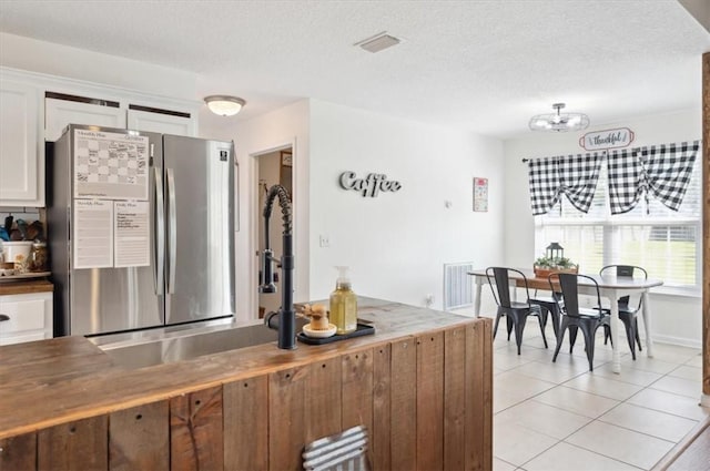 kitchen featuring white cabinets, light tile patterned floors, a textured ceiling, and stainless steel refrigerator