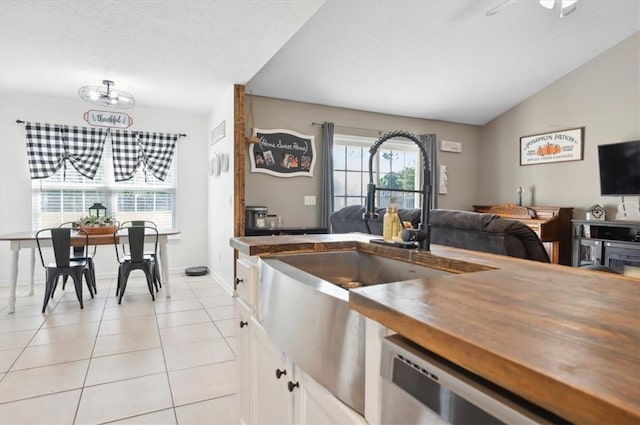 kitchen with dishwasher, white cabinets, sink, vaulted ceiling, and light tile patterned flooring