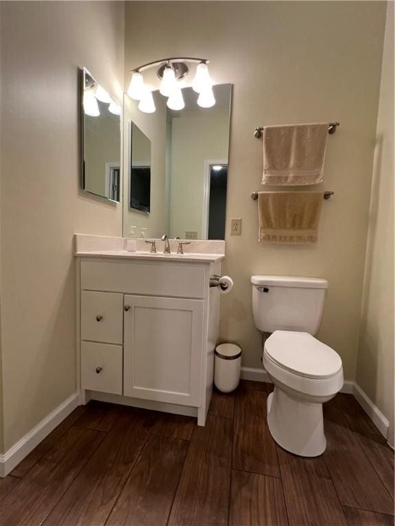 bathroom with baseboards, toilet, wood finished floors, and vanity