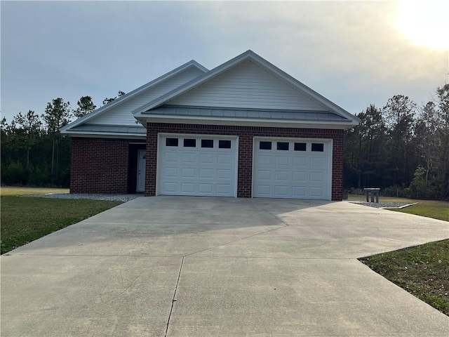 view of front of house with driveway, a standing seam roof, a front yard, an attached garage, and brick siding