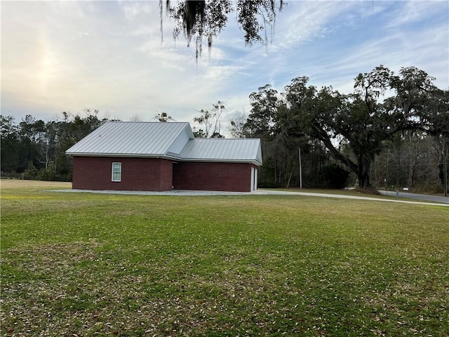 view of home's exterior featuring metal roof, a lawn, an attached garage, and brick siding