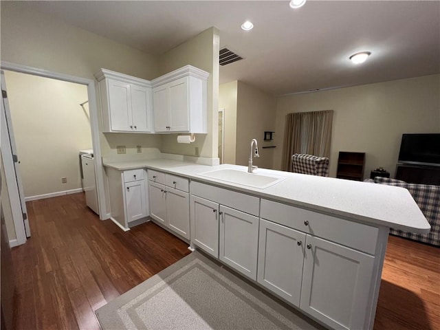 kitchen with visible vents, a sink, a peninsula, white cabinets, and light countertops