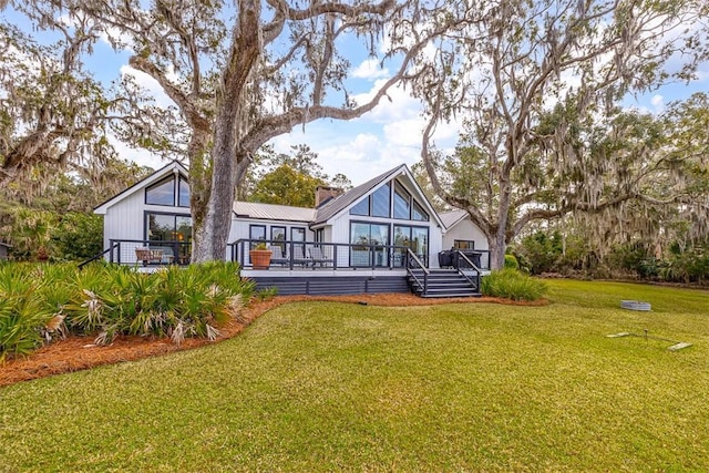 rear view of property featuring a deck, a lawn, and a chimney