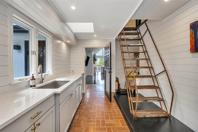 interior space with brick floor, a skylight, recessed lighting, a sink, and wood walls