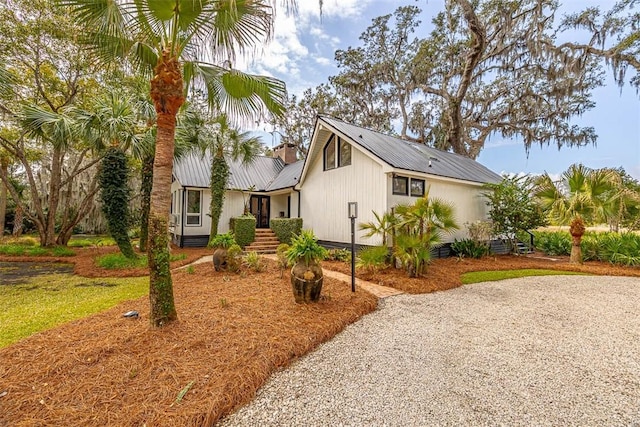 view of front of house featuring gravel driveway, metal roof, and a chimney